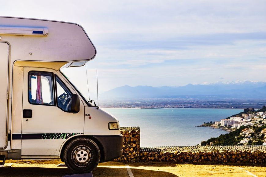 Camper van parked by a seaside overlook with blue water and distant mountains at sunset
