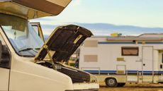 Open car hood beside a camper trailer in a sunlit lot
