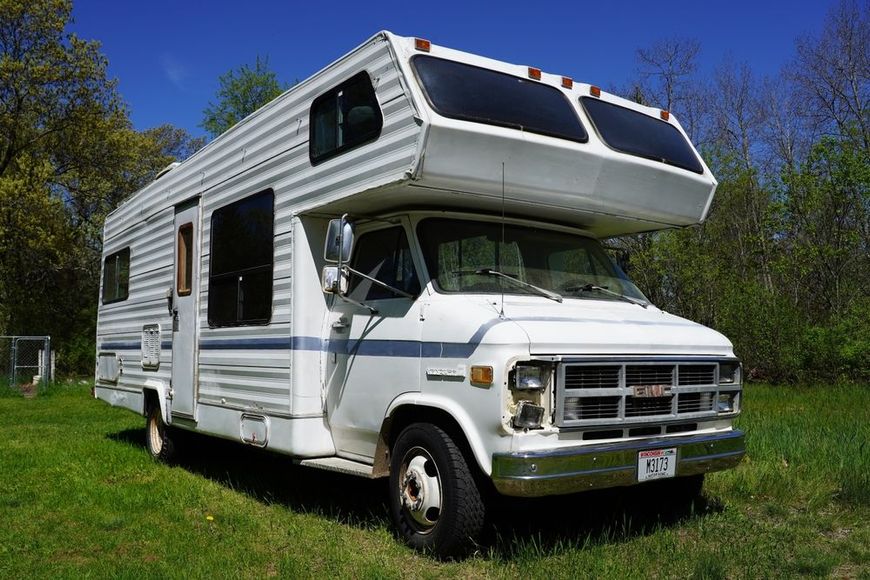 White RV camper parked on grass beside trees under a blue sky