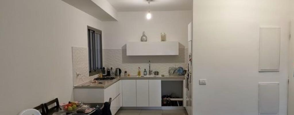 מטבח עם ארונות לבנים ובתוכו שולחן וכיסאות.