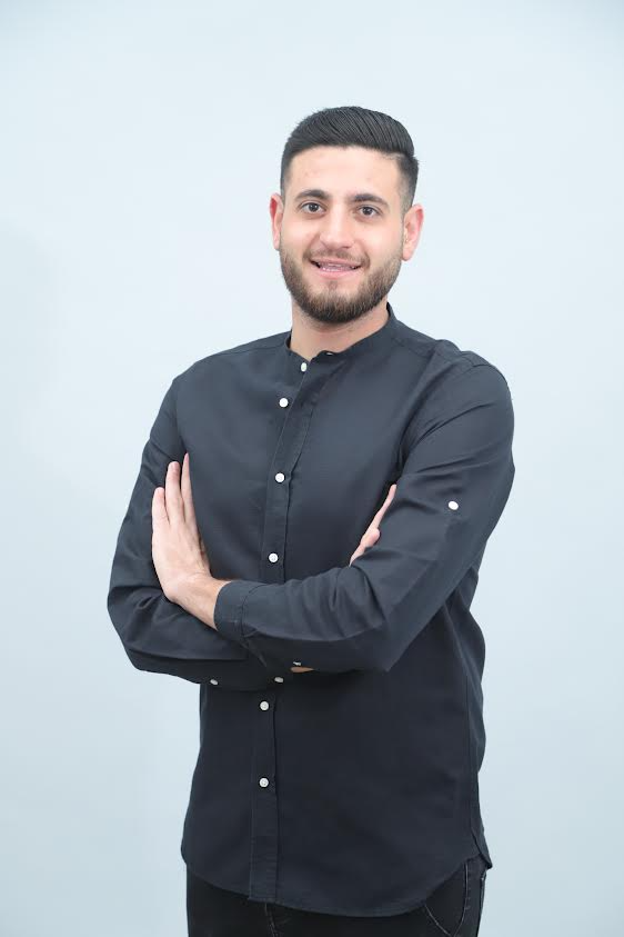 גבר בחולצה שחורה עומד בזרועותיו שלובות.