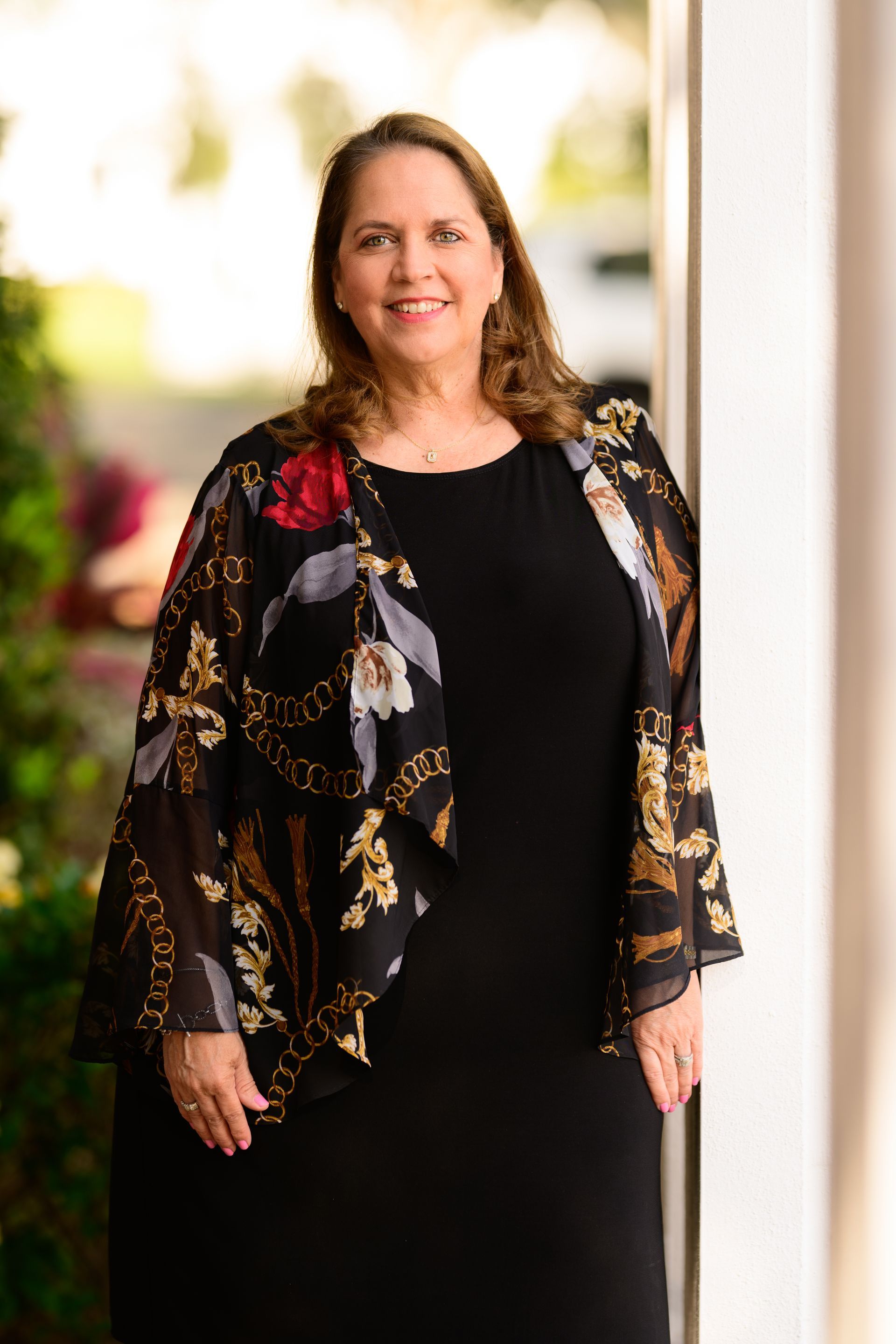Woman in a black dress with a floral shawl standing outdoors, smiling at the camera.