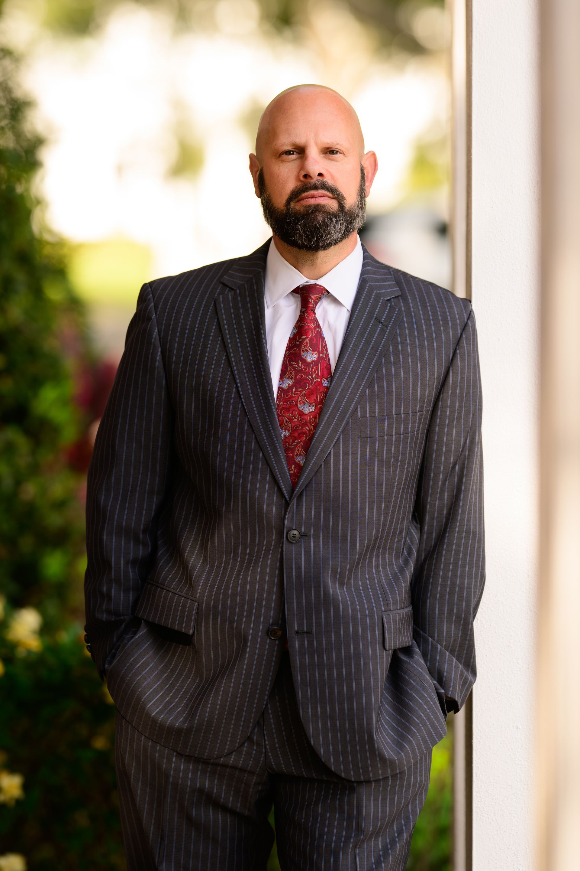 Man in a dark pinstripe suit with a red tie standing outdoors by a column