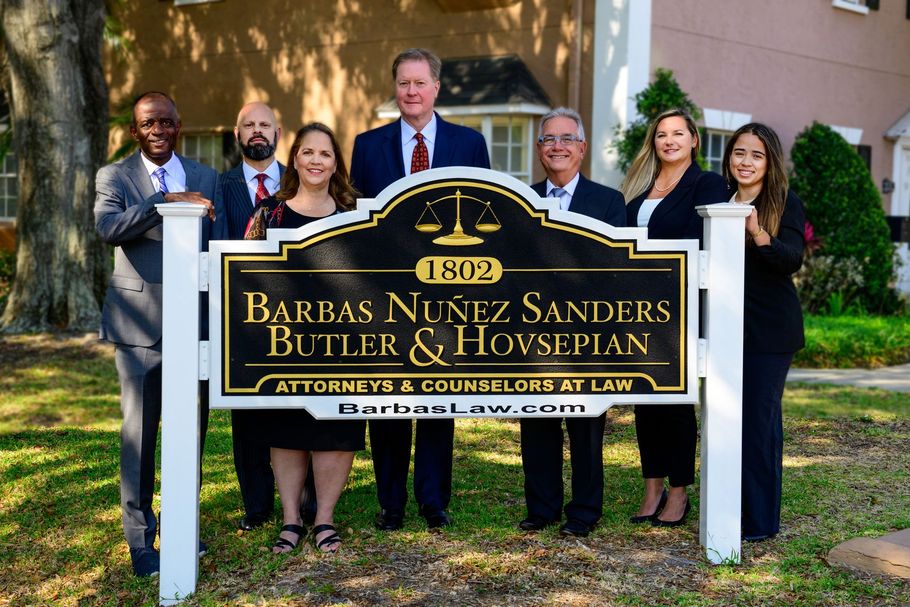 Group of people standing behind a law firm sign outdoors in front of a brick building and trees