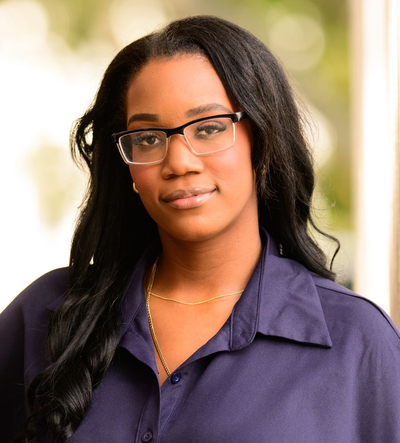 Portrait of a person wearing glasses and a purple blouse against a blurred outdoor background