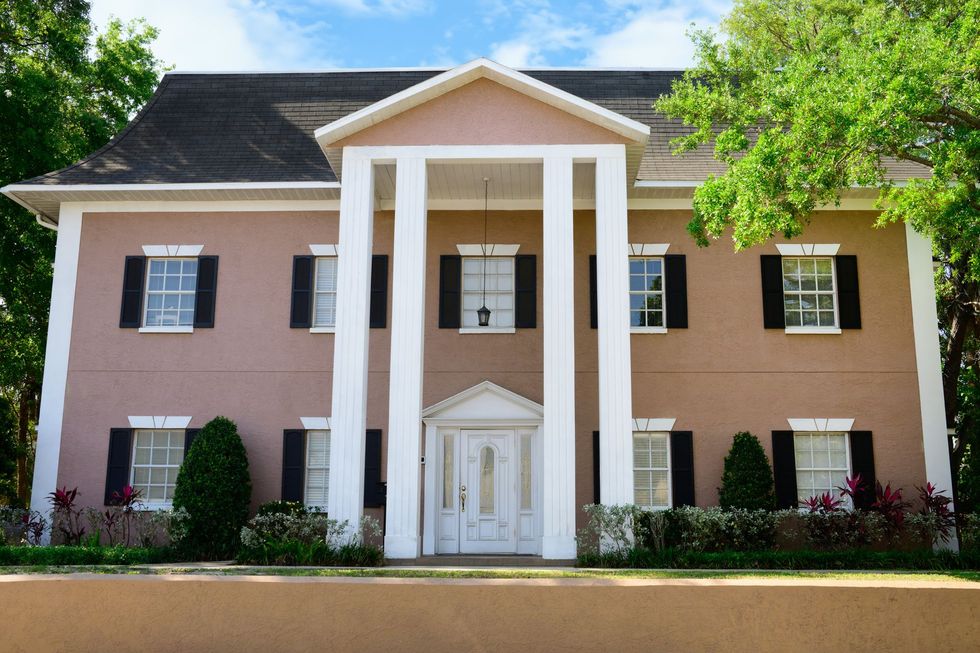 Pink colonial-style house with white columns, black shutters, and a manicured front lawn