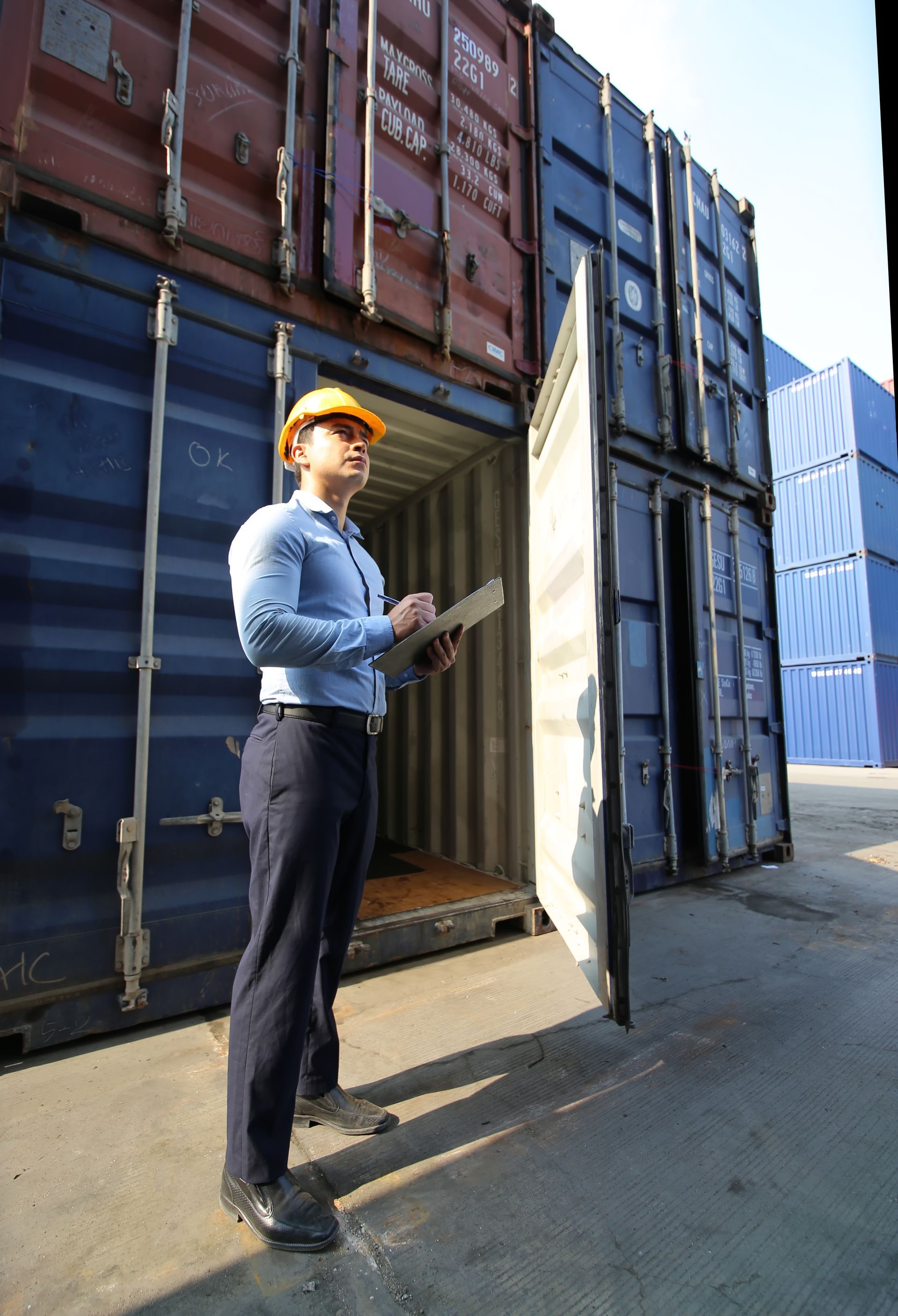 Worker in a hard hat standing by an open shipping container at a port.