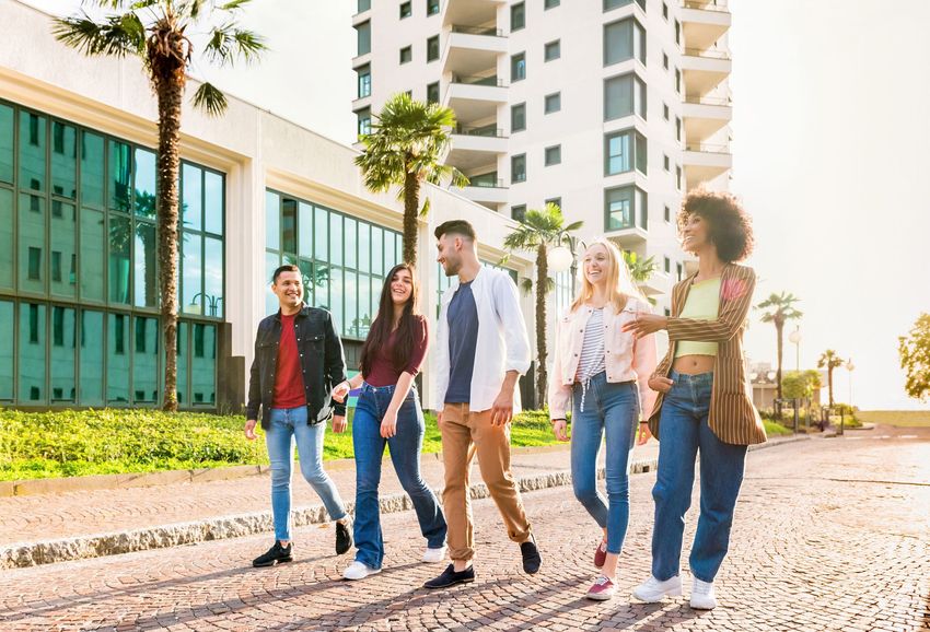 Five students walking together on a sunny campus path beside modern buildings and palm trees