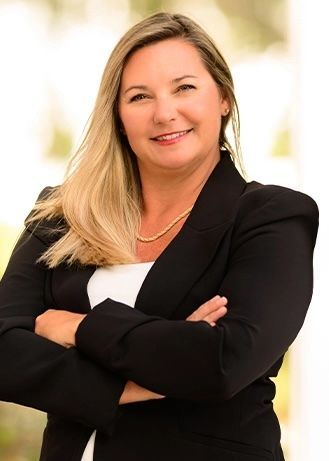 Smiling professional in black blazer with arms crossed against a bright blurred background