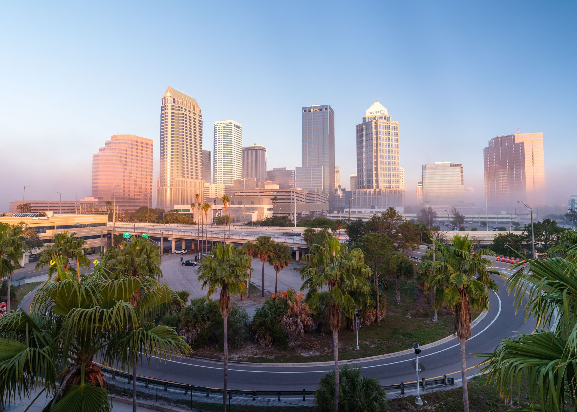 Palm-lined road overlooking modern city skyline in soft morning mist at sunrise