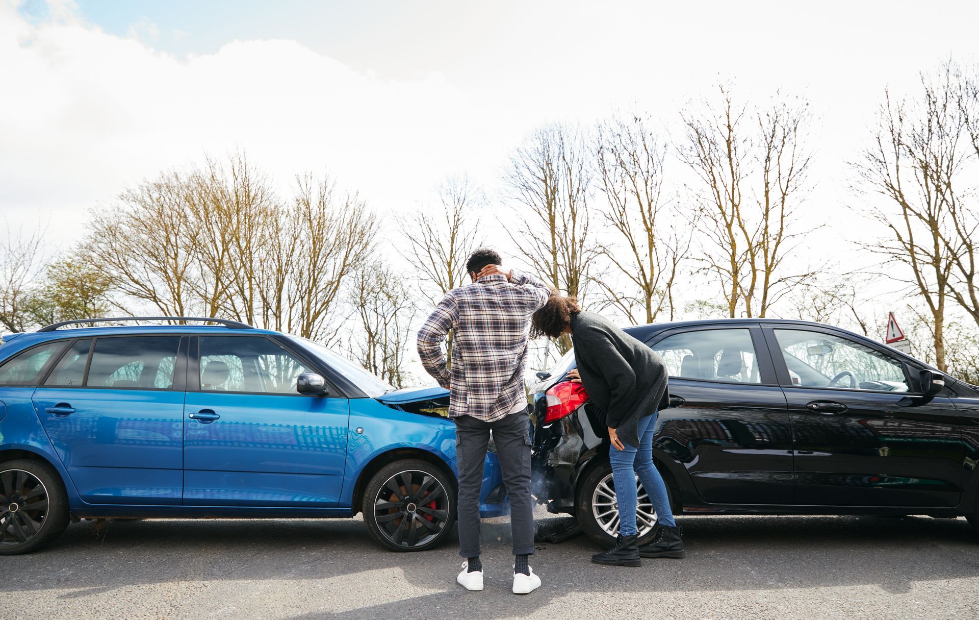 Two people inspecting a black car between a blue car and a black car on a roadside