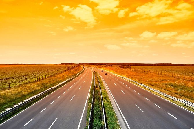 Autostrada deserta che si snoda attraverso campi pianeggianti sotto un cielo dorato al tramonto.