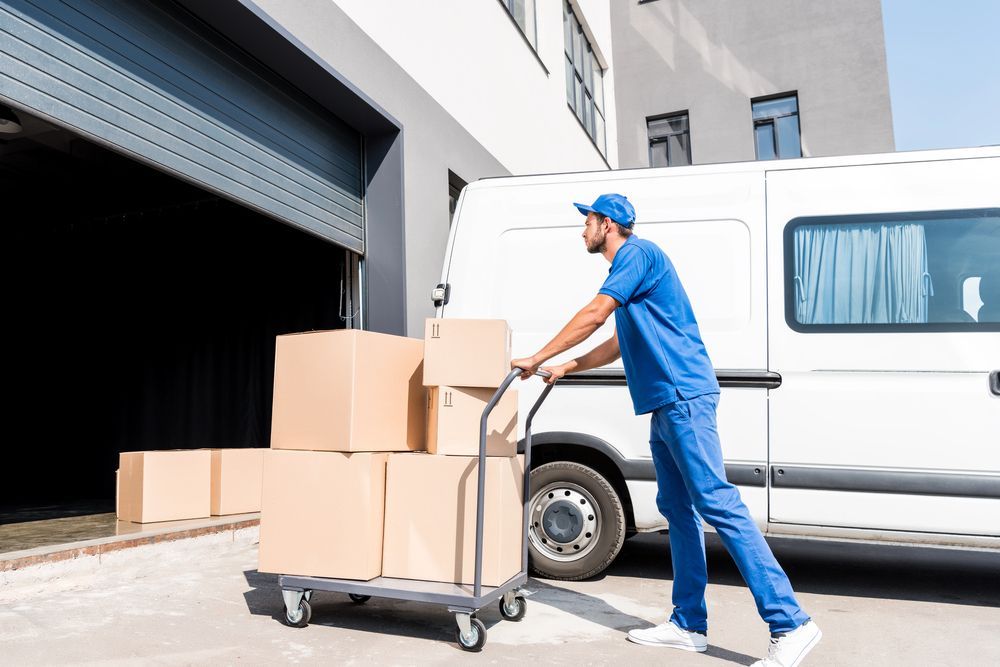 Un addetto alle consegne in uniforme blu scarica scatole di cartone da un camion presso la banchina di un magazzino.
