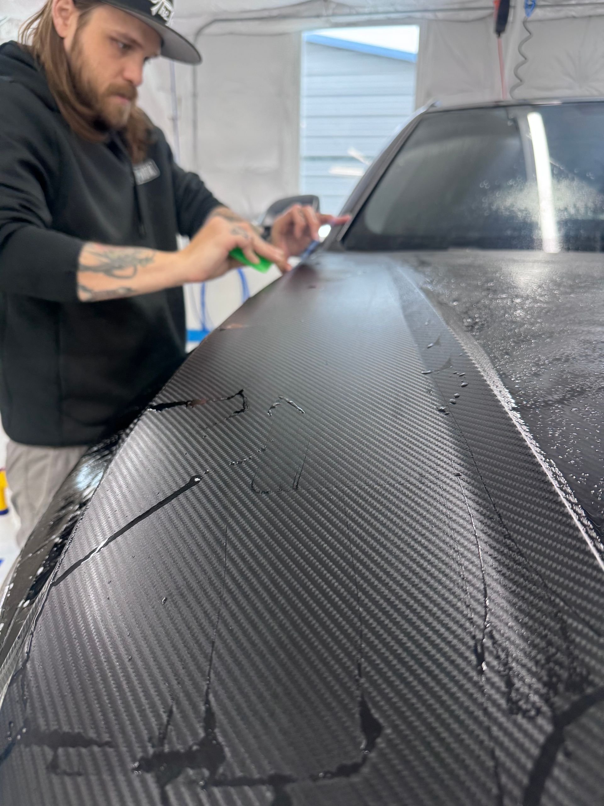 A man is applying a protective film to the hood of a car.