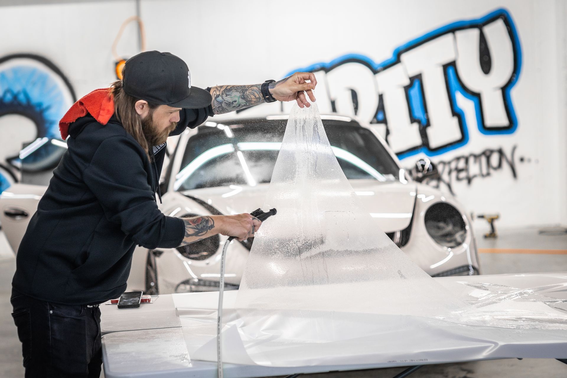 A man is applying a protective film to the hood of a car.
