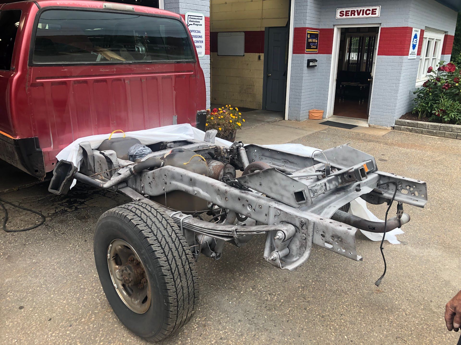 Red pickup truck with the bed removed, revealing the chassis, parked near a service building. | Rose Brothers Garage