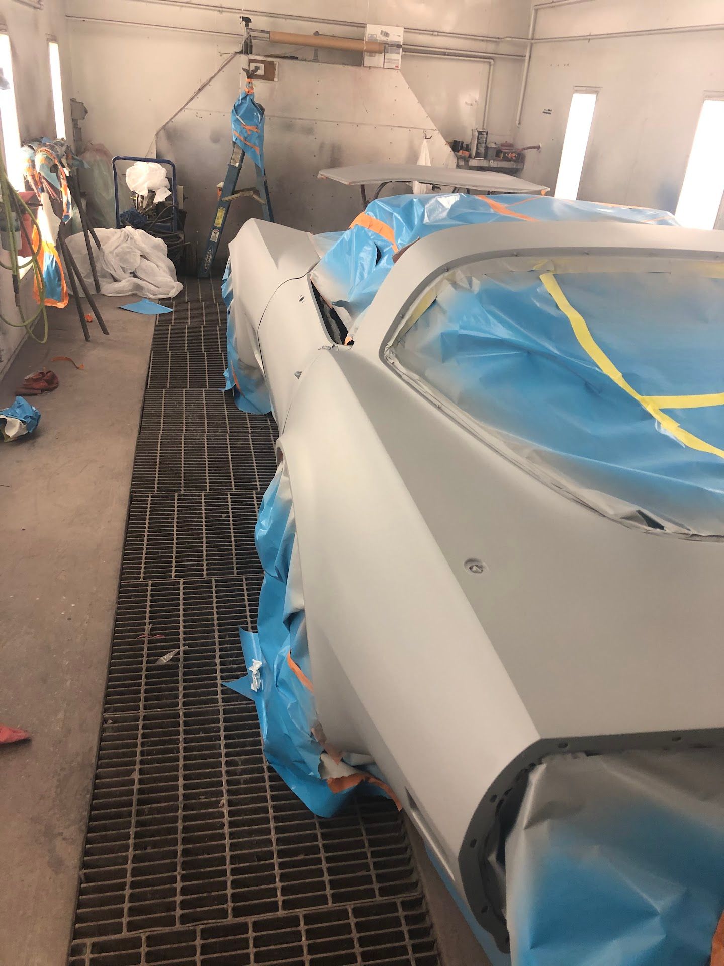 Car in a body shop, prepped for painting. Blue tape protects glass and trim. Gray primer on the body. | Rose Brothers Garage