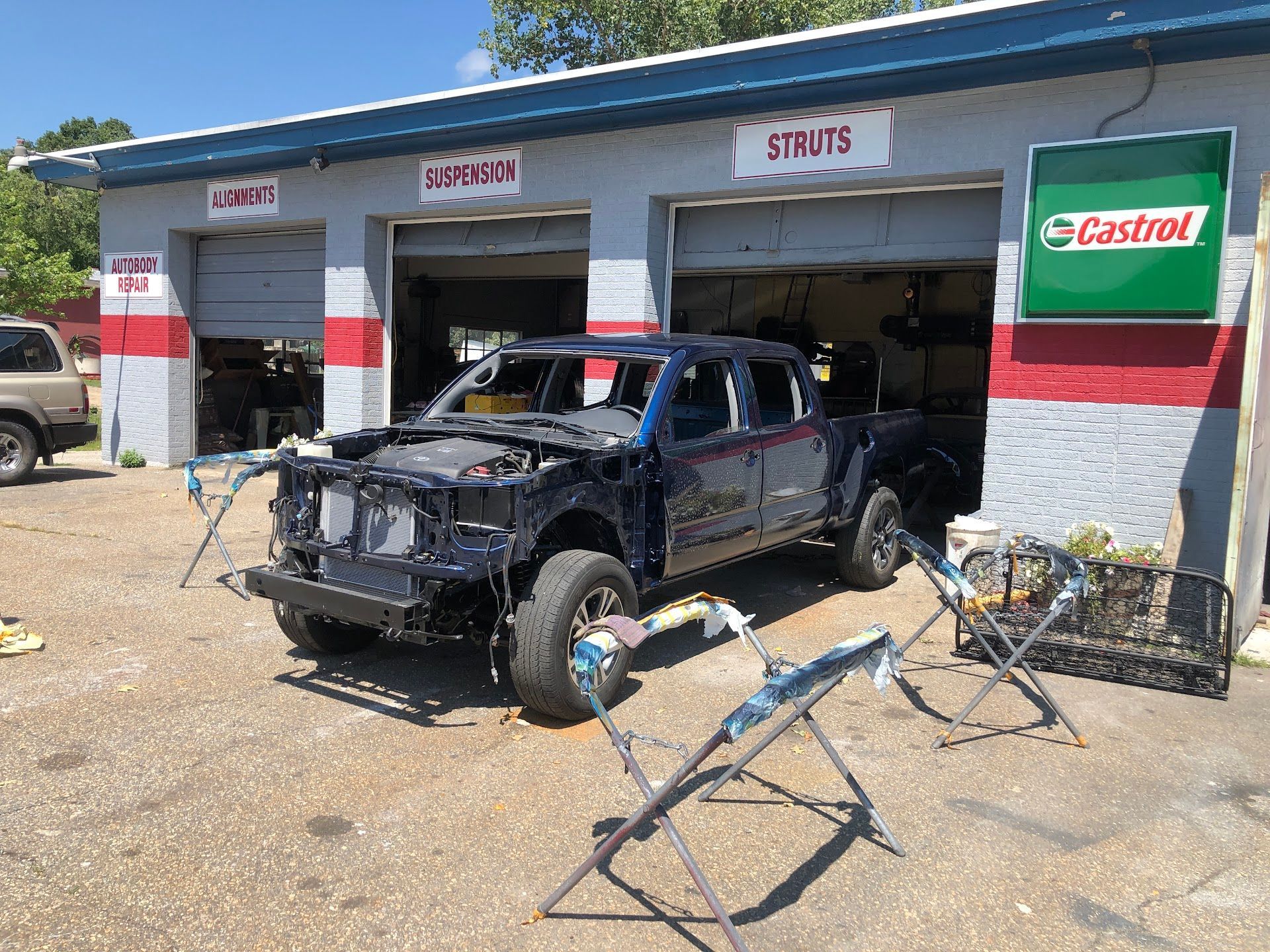 A dark blue pickup truck stripped for repairs in front of a garage with signs for