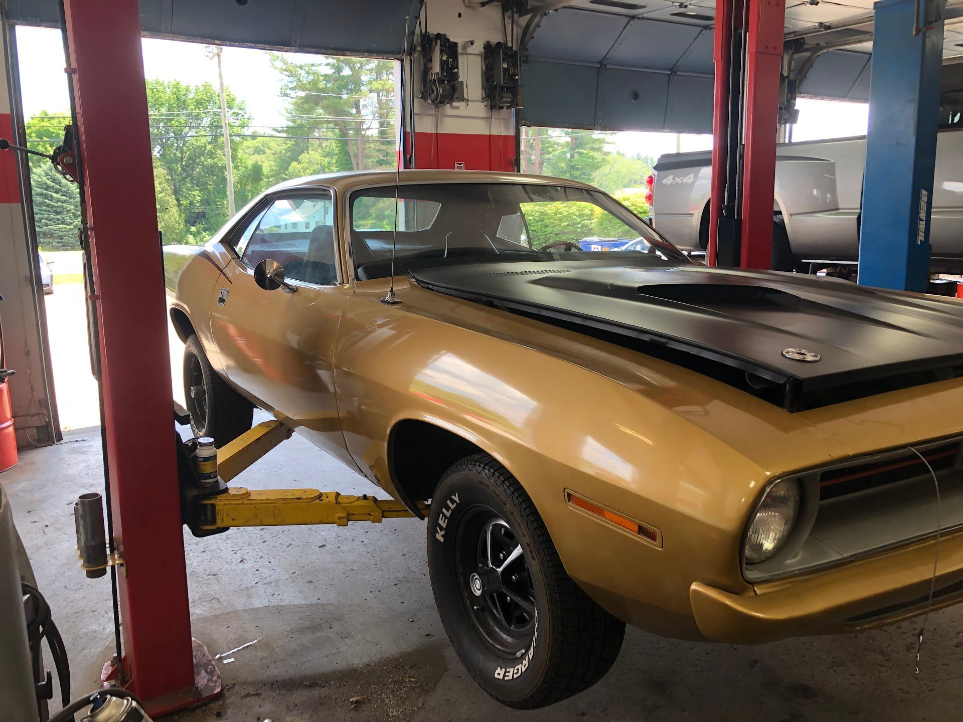 Gold vintage muscle car on a lift in a garage, black hood. | Rose Brothers Garage