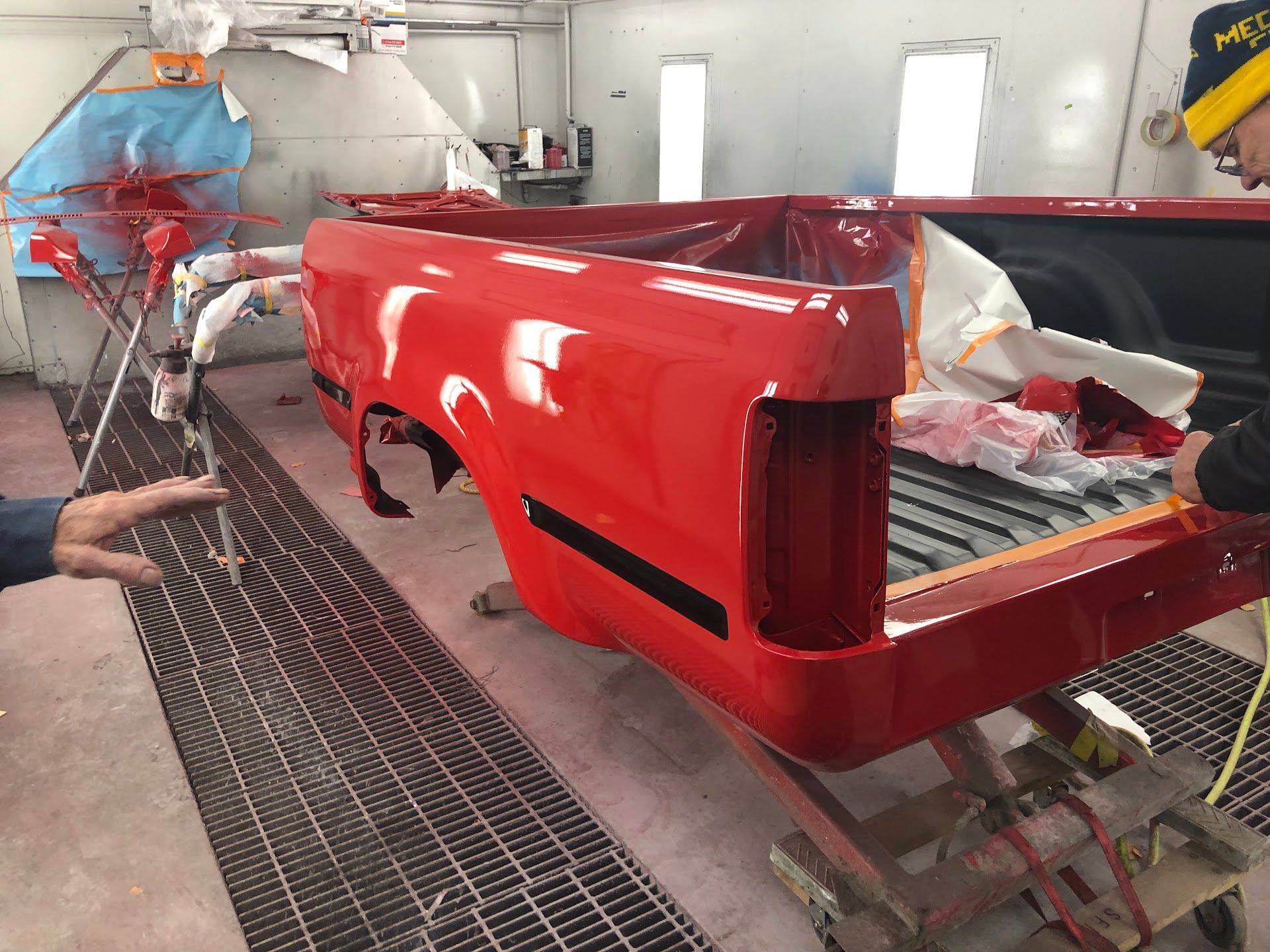 Red truck bed in a paint booth, freshly painted. Two people nearby. | Rose Brothers Garage