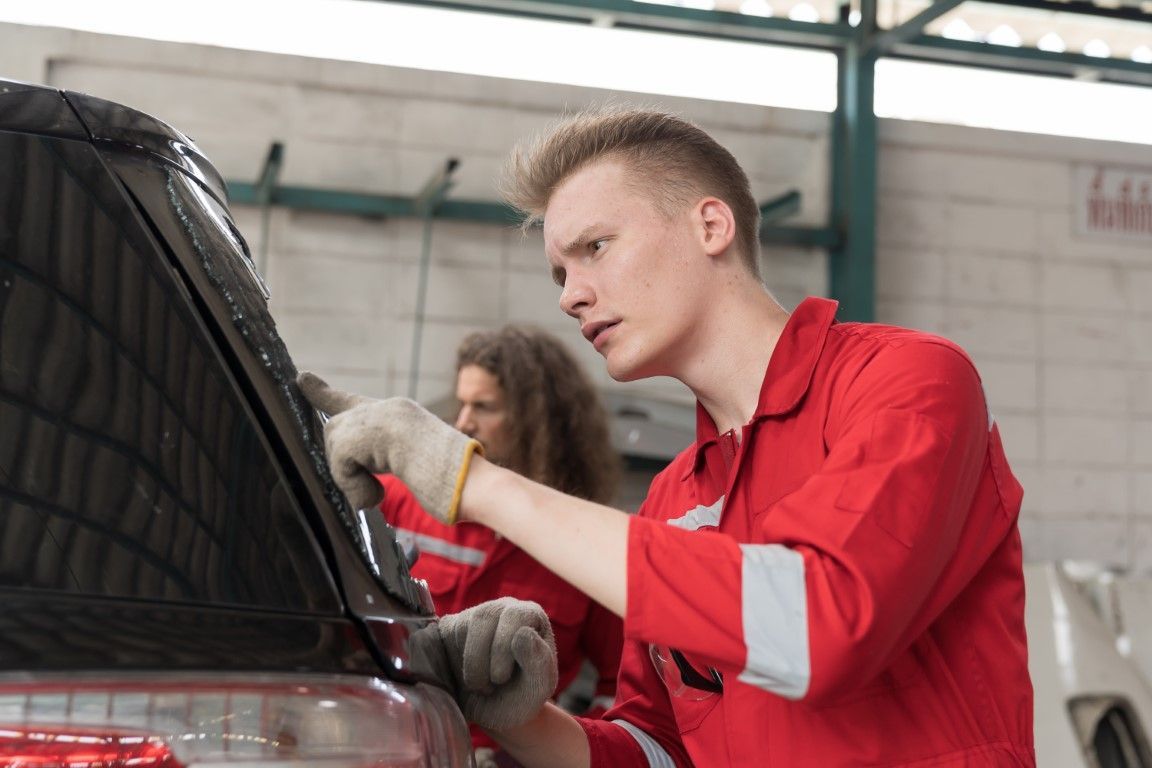 Mechanic in red shirt checks car engine with hood open in a garage
