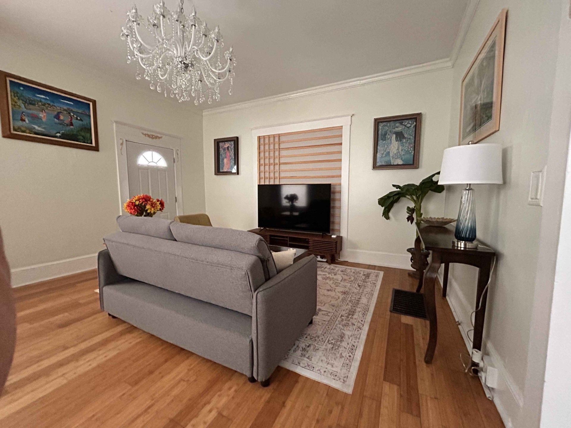 A living room with a couch , television , lamp and chandelier.