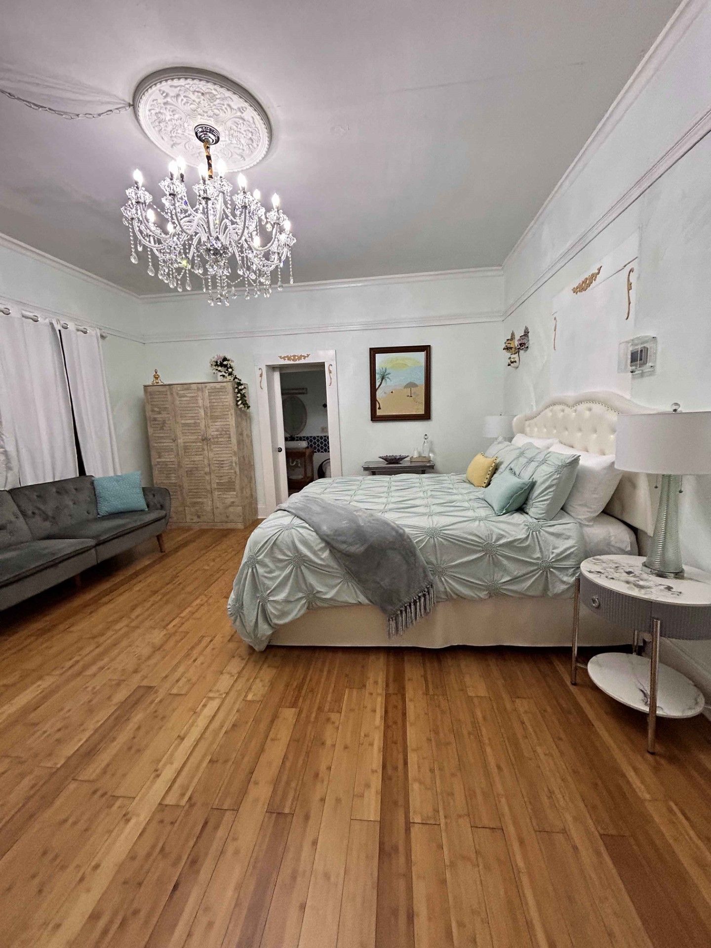 A bedroom with a bed , couch , nightstand and chandelier.