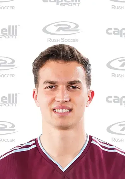 A young man wearing a maroon soccer jersey is smiling for the camera.