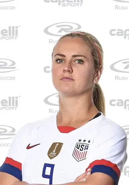 A woman wearing a usa soccer jersey stands with her arms crossed