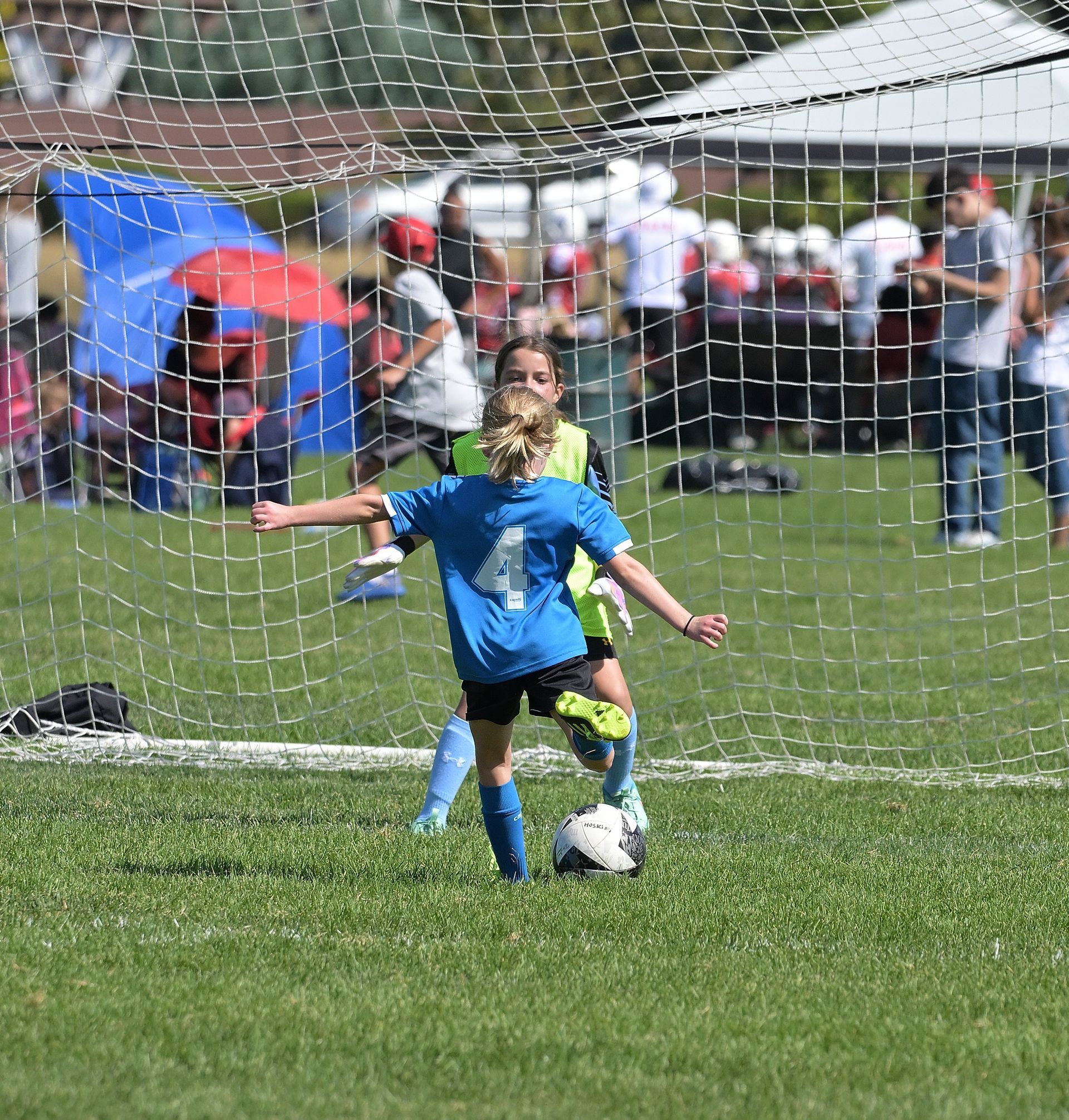 A girl in a blue shirt with the number 4 on it kicks a soccer ball
