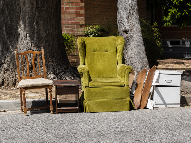 Old green armchair, wooden chair, shelving, and cabinet pieces set out for junk removal.