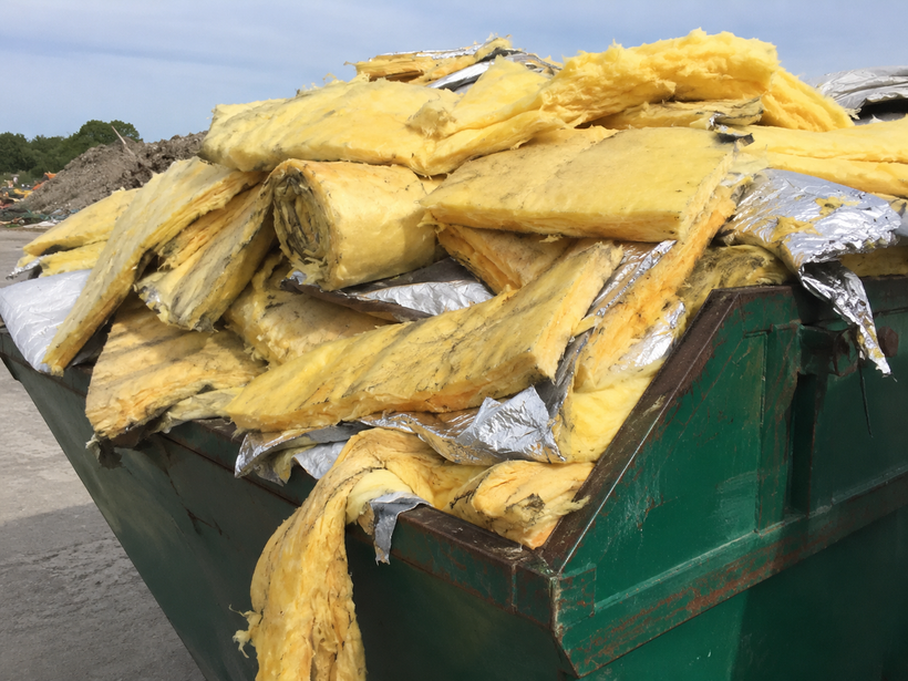 Yellow fiberglass insulation overflowing from a green construction dumpster.