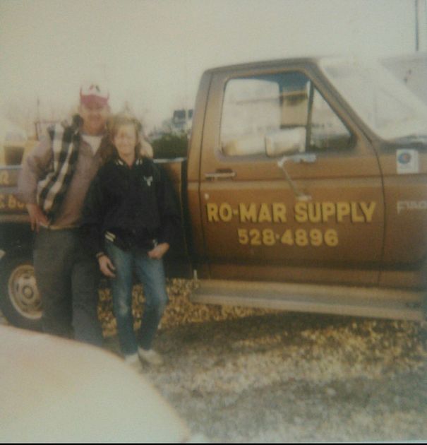 Two people standing beside a brown RO-MAR SUPPLY pickup truck outdoors