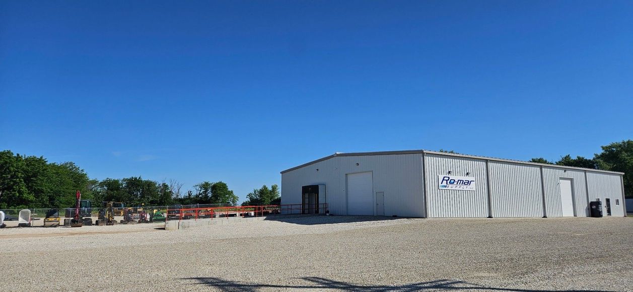 Gravel lot with a white industrial building under a clear blue sky.