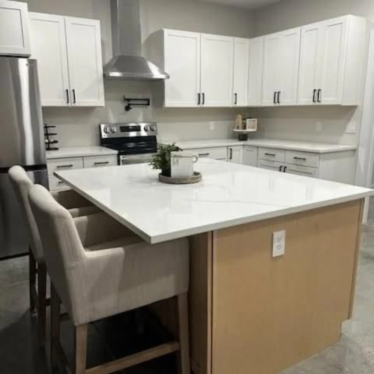 White kitchen with island and bar stools, stainless steel appliances, light wood accents.