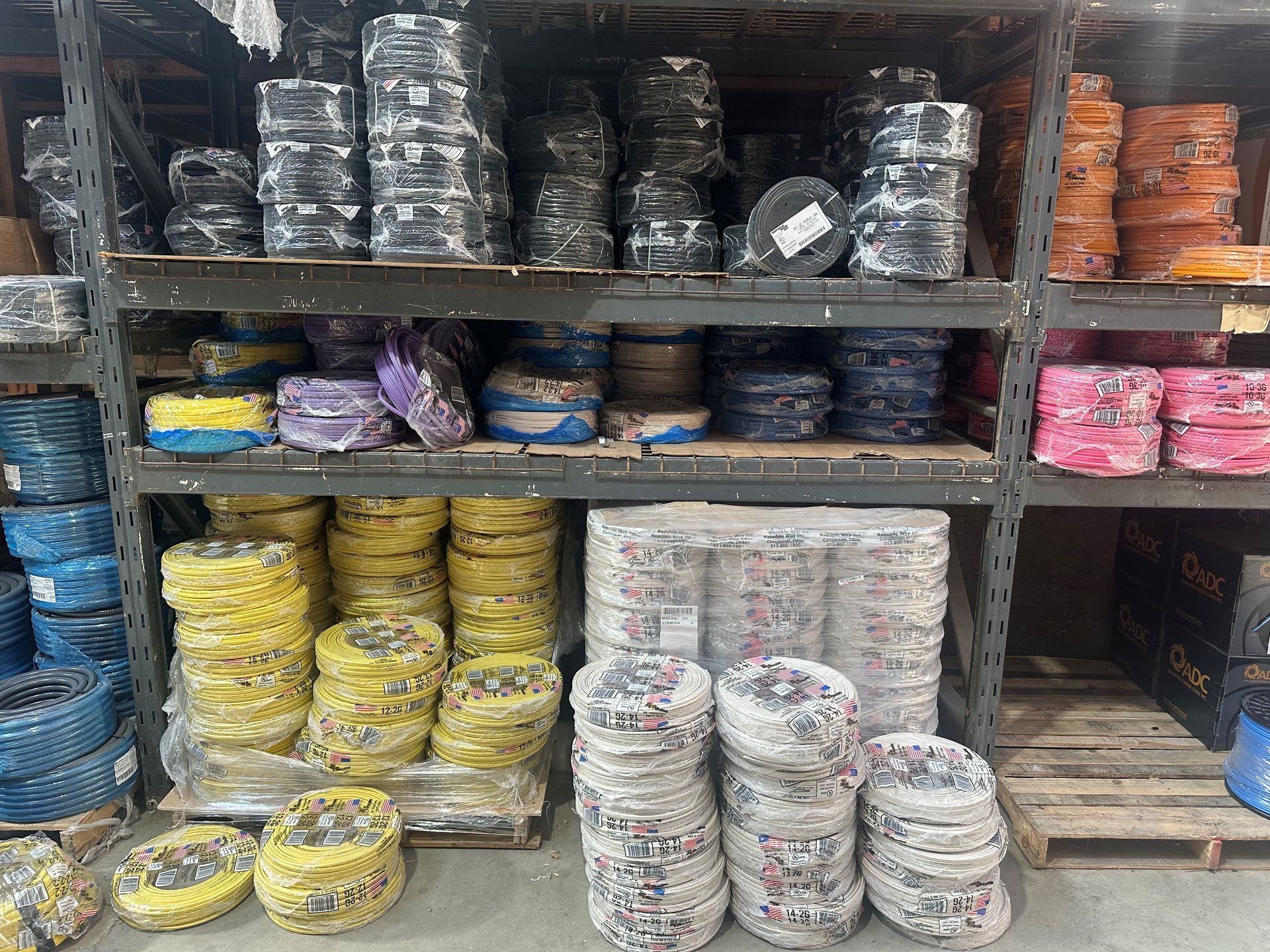 Shelves stacked with wrapped rolls of materials in black, yellow, white, and pink bundles in a store aisle