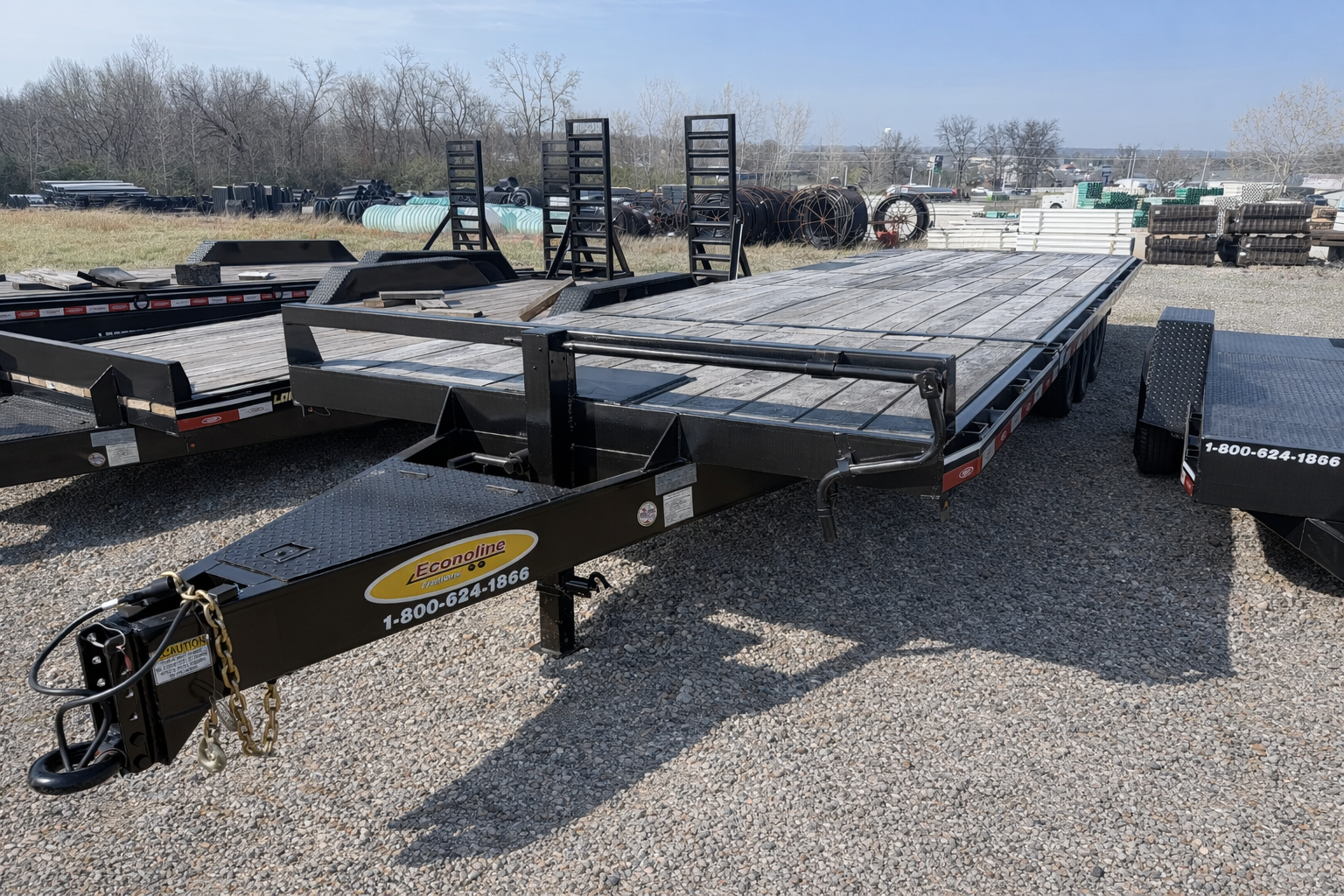 Black flatbed car trailer parked on gravel in a lot with trees in the background