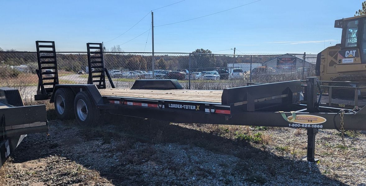 A black trailer with ramps, parked on gravel, with a Cat bulldozer visible on the right.