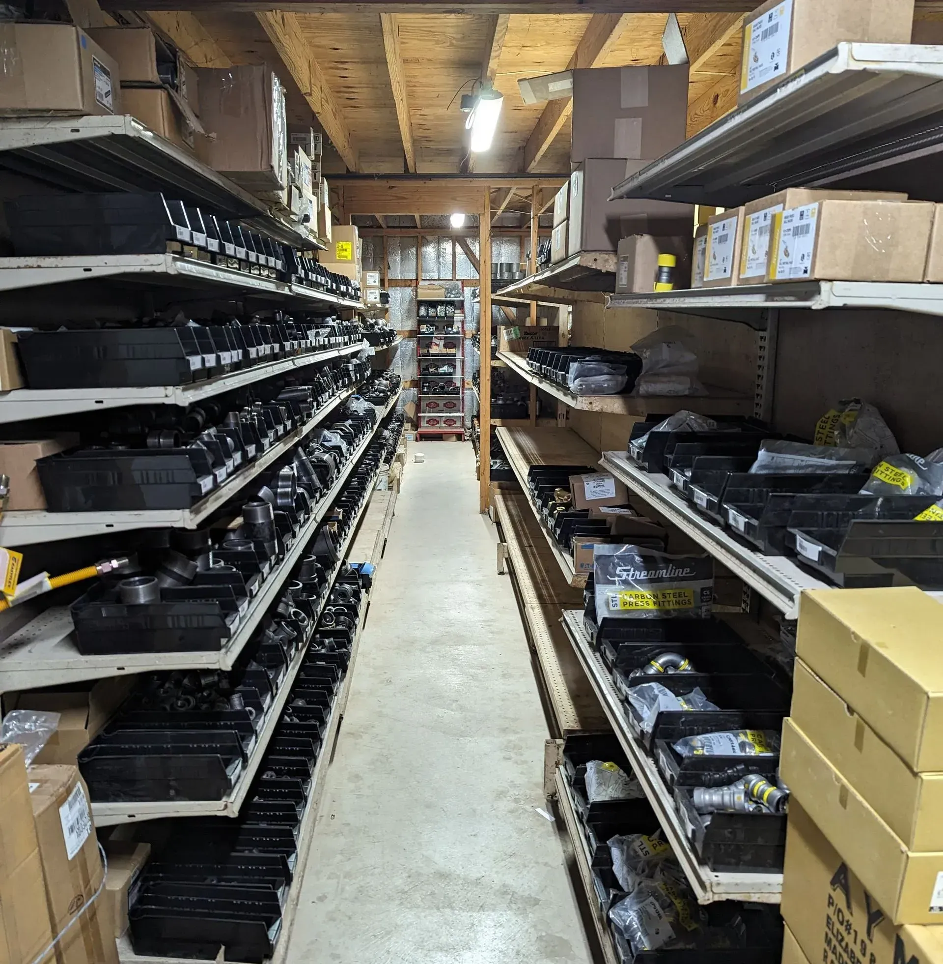 Warehouse shelves filled with black boxes and other items. Narrow aisle, overhead lighting.