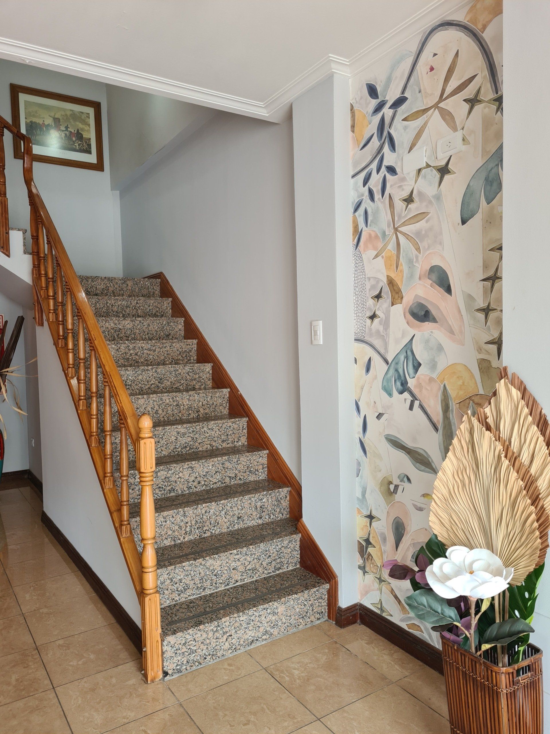 Escalera con escalones de granito y pasamanos de madera. Papel pintado floral en la pared.