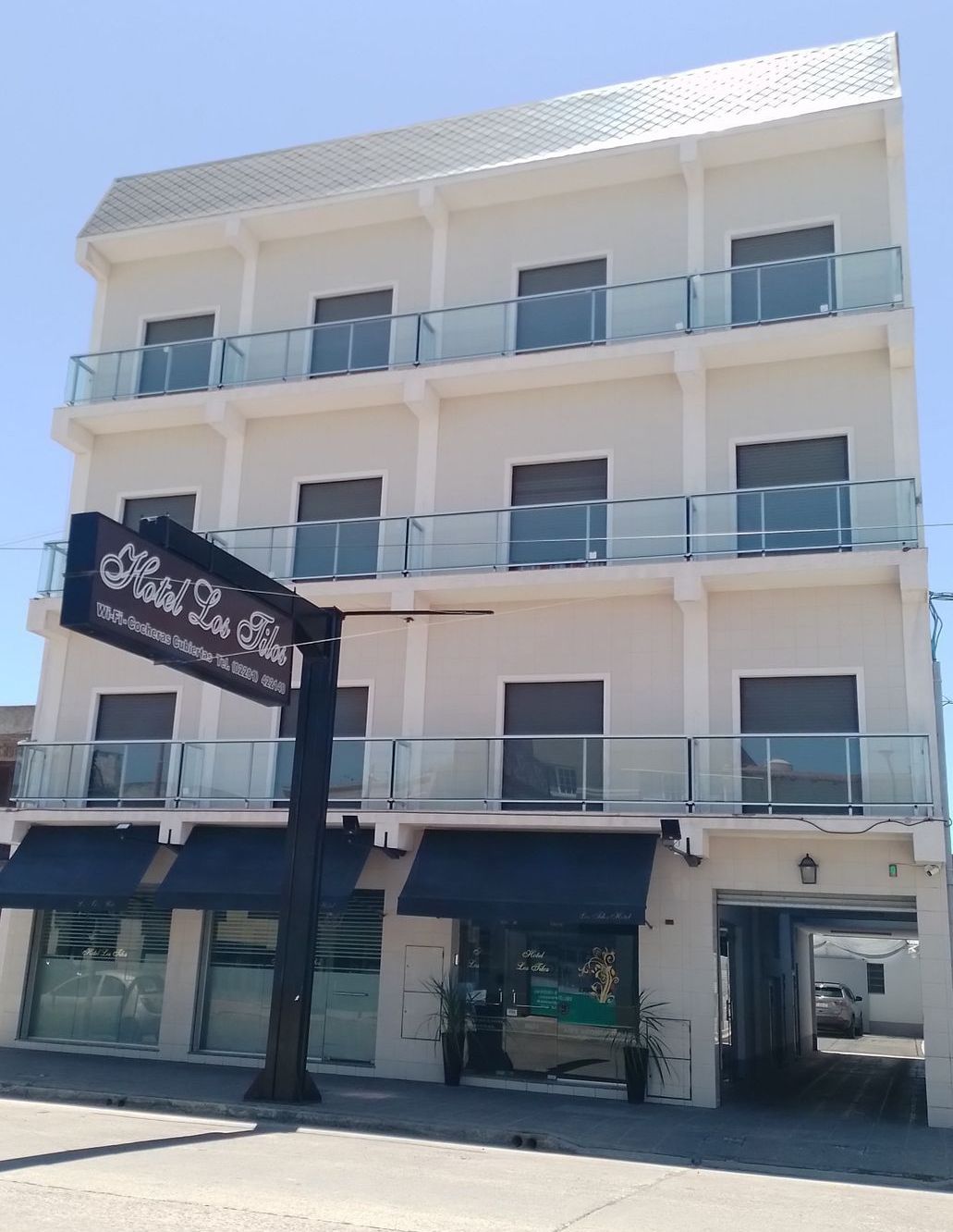 Un edificio blanco de tres pisos con balcones de vidrio, un cartel que dice
