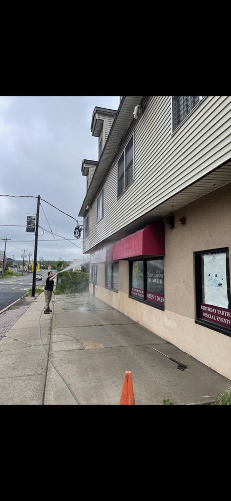 Person pressure washing a commercial building's exterior on a sidewalk next to a street.