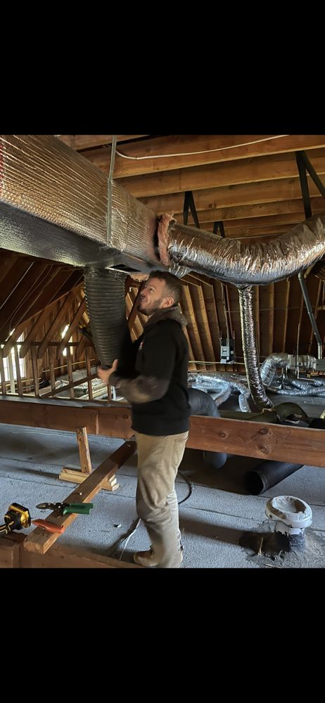Man installing HVAC ductwork in an attic.