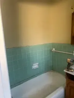 A bathroom with green tiles and a bathtub.