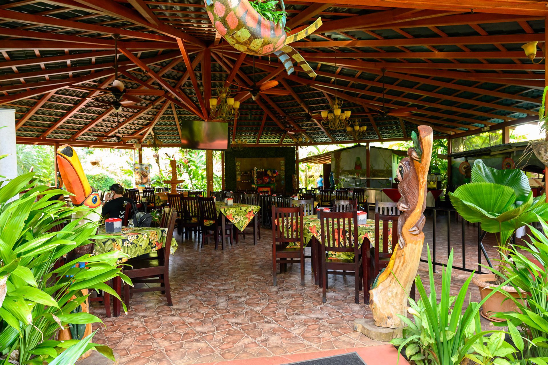 Restaurant with wooden beams, tables, chairs, and lush plants.