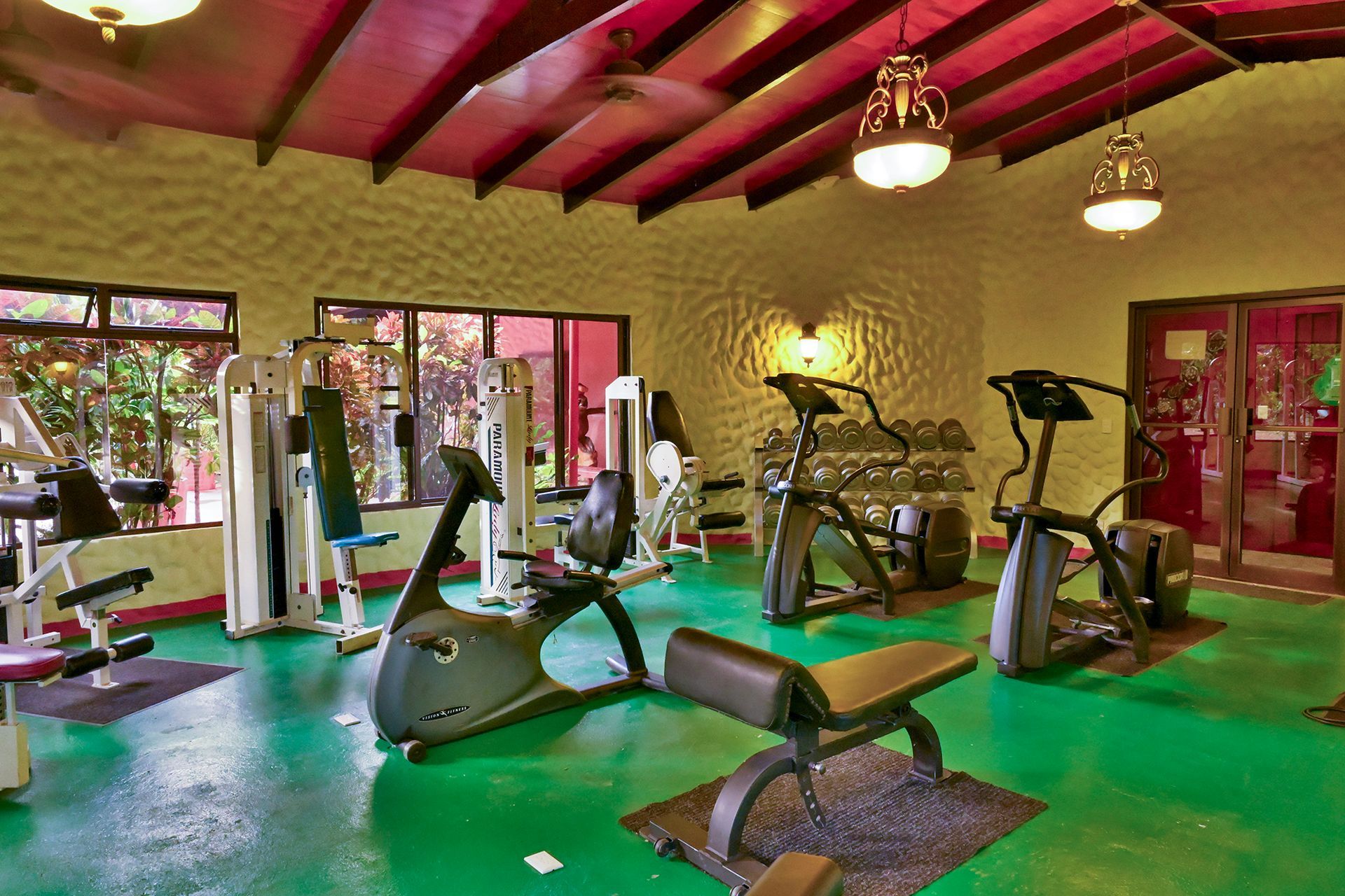 Gym with exercise machines on a green floor, with red-painted ceiling and arched windows.