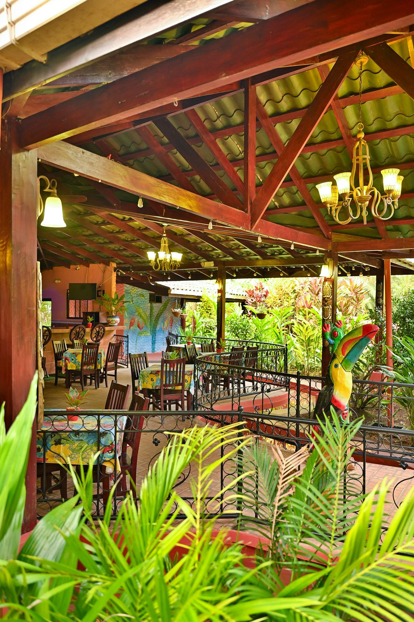 Covered outdoor restaurant with tables, chairs, and tropical foliage.