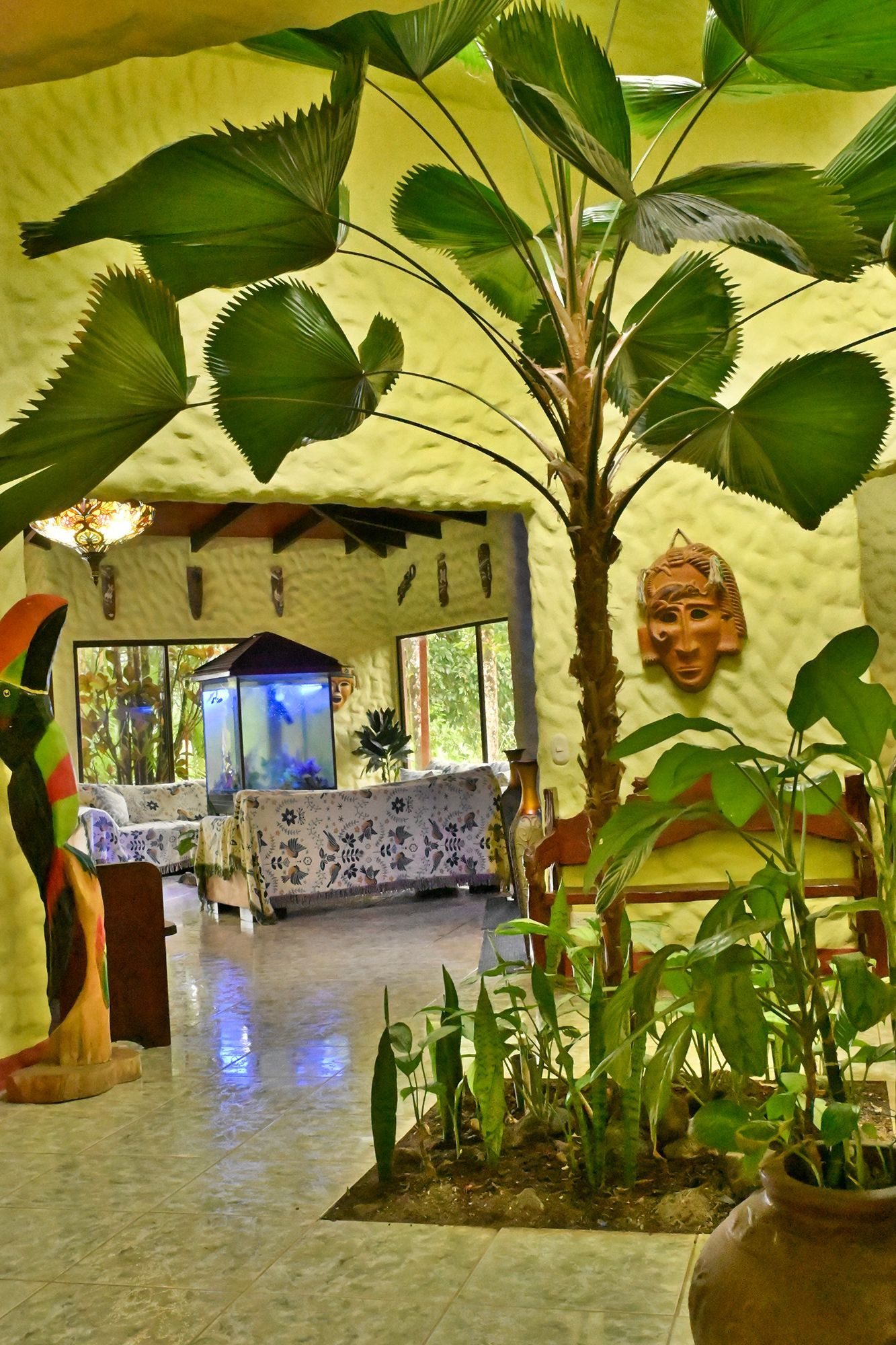 Interior with tropical plants, including palm fronds, a wood sculpture, and decorative masks.