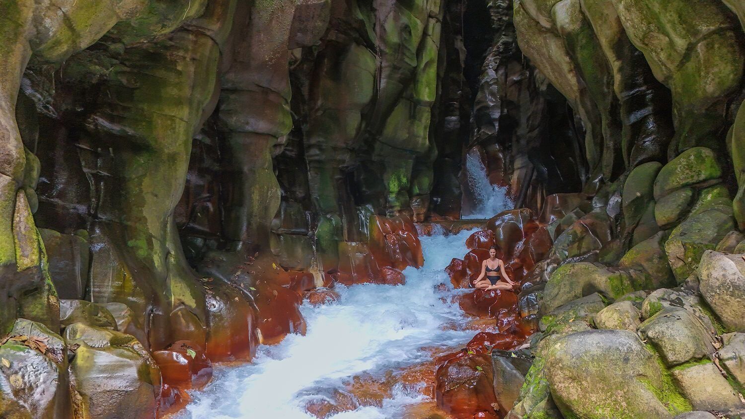 A person is meditating in a cave next to a waterfall in Costa Rica.