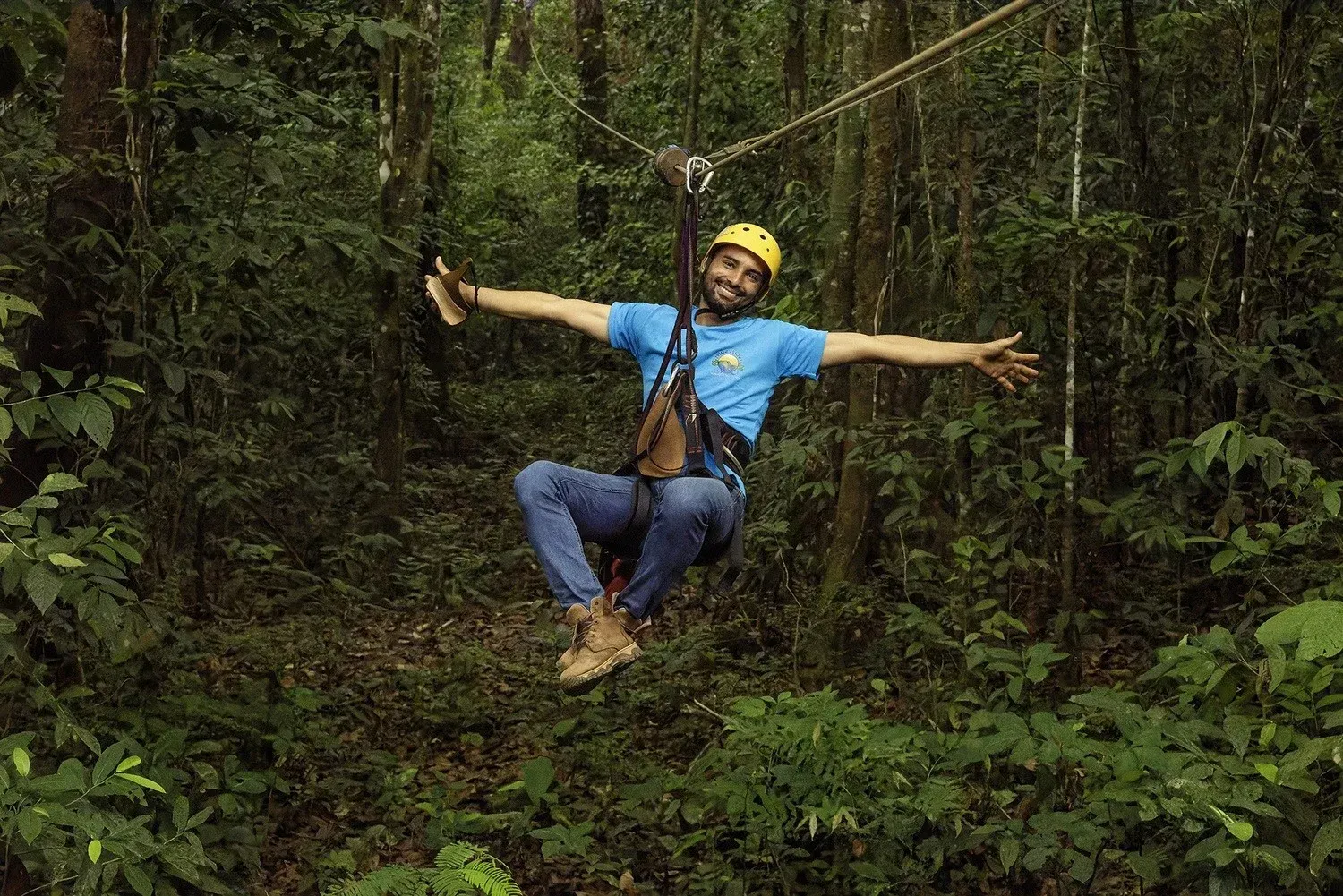 A man is flying through the air on a zip line in the woods in Costa Rica.